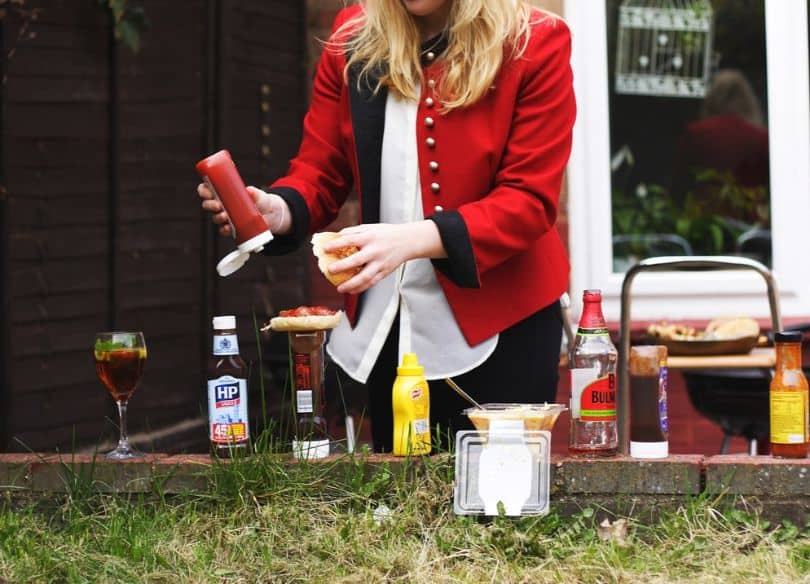 person putting condiments on burger bun