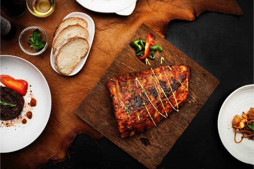 BBQ joint on wooden chopping board with satellite plates and dishes