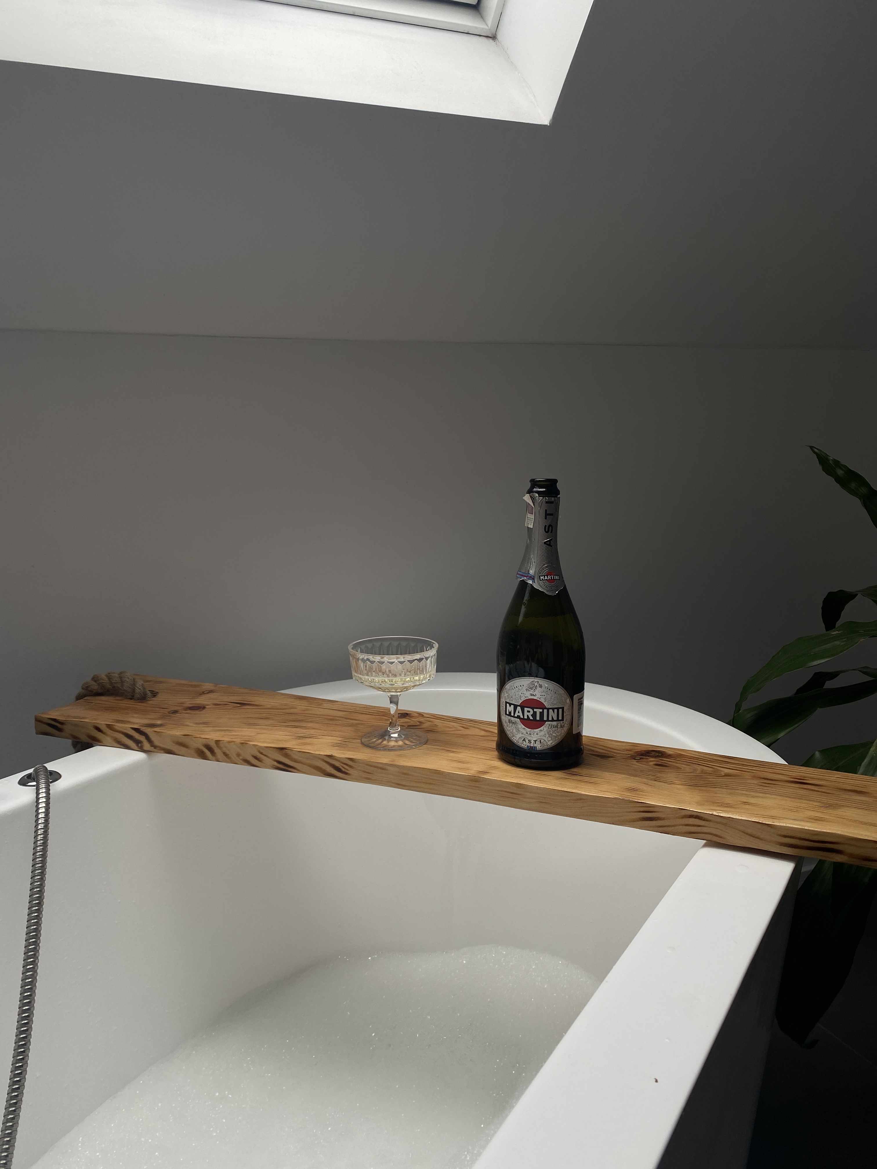 A bottle of wine and a goblet on a bathtub caddy