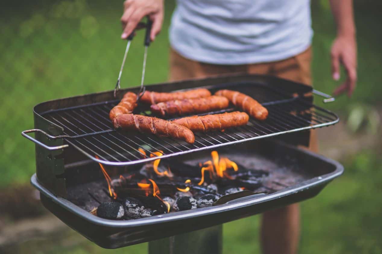 bottom half of someone at a small raised charcoal grill with sausages on top