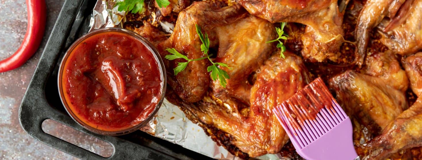 bbq sauce and wings in cooking tray with brush