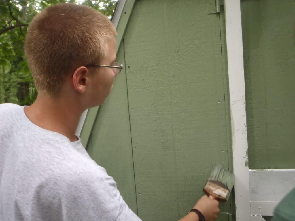 A man painting a shed in green colour