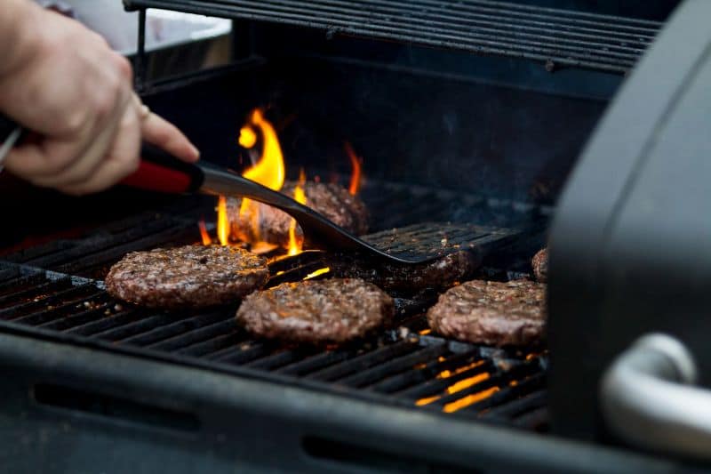 hand patting down burgers on a charcoal grill with spatula