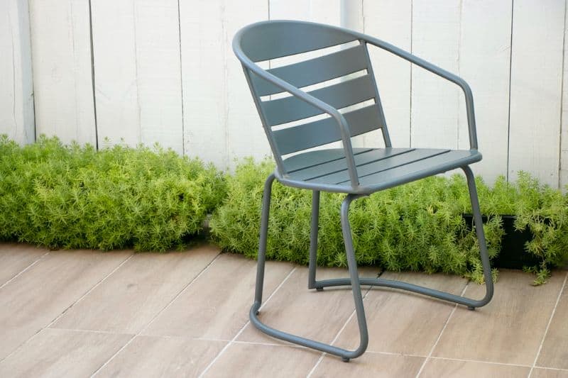 aluminium chair on patio tiles next to low green bushes