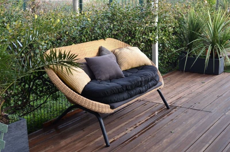 natural rattan loveseat with cushions on deck surrounded by plants