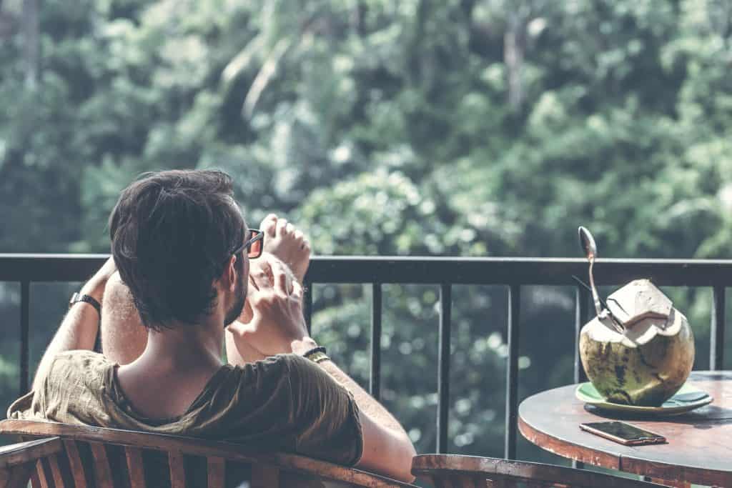over the shoulder of Man with feet up on balcony with a coconut on the table