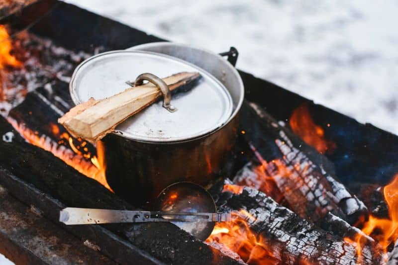 A pot on the grill with a wood stake through the handle
