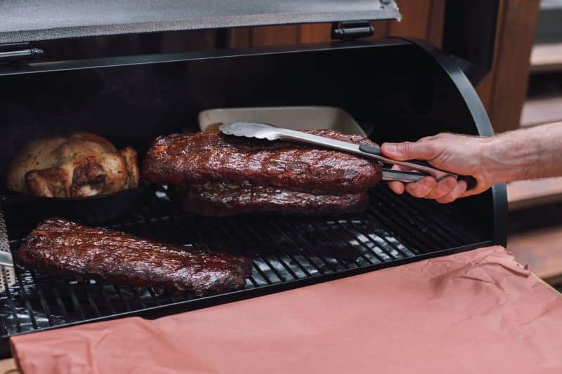 hand with tongs taking meat out a smoker