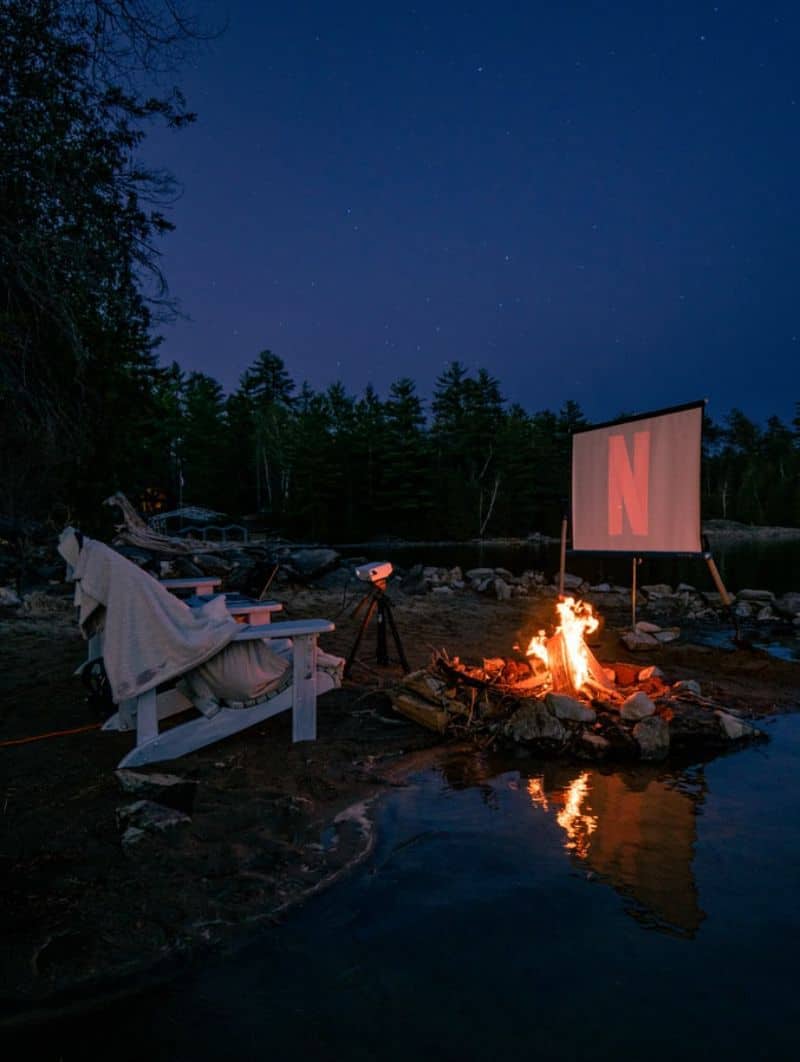 A cosy set-up for an outdoor home cinema with a bonfire and large Netflix logo on projector