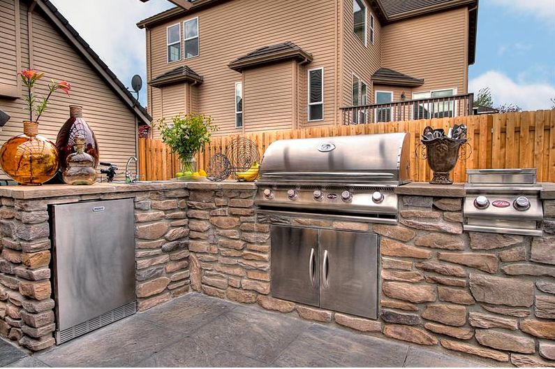 A built-in gas BBQ island with natural stone construction and ample counter space, surrounded by cedar fencing.