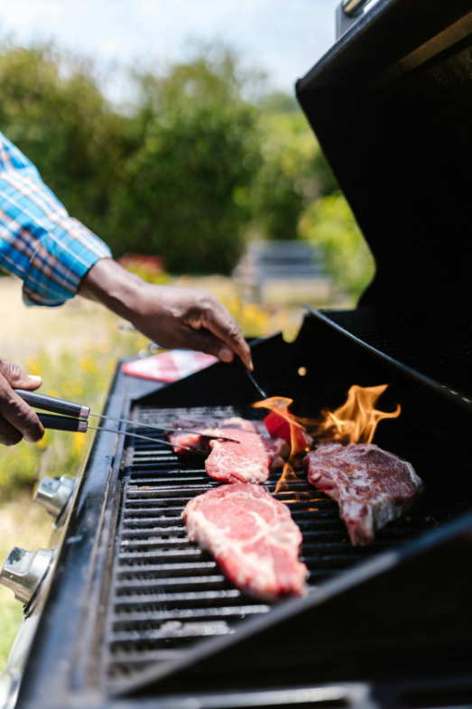 Close-up of meat grilling on a BBQ with visible flames and smoke.