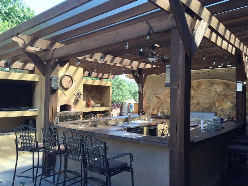 A pergola style outdoor kitchen space with built-in grill, countertop and bar stools