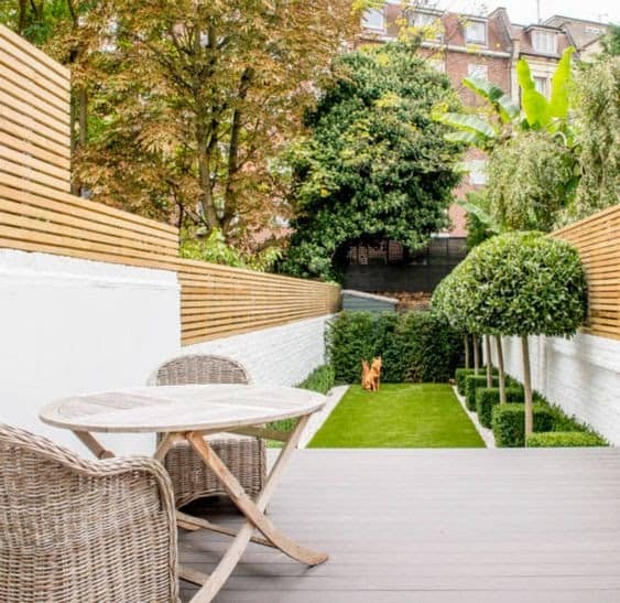 A long, narrow garden with a comfortable seating area on the deck, modern fencing and a section of grass