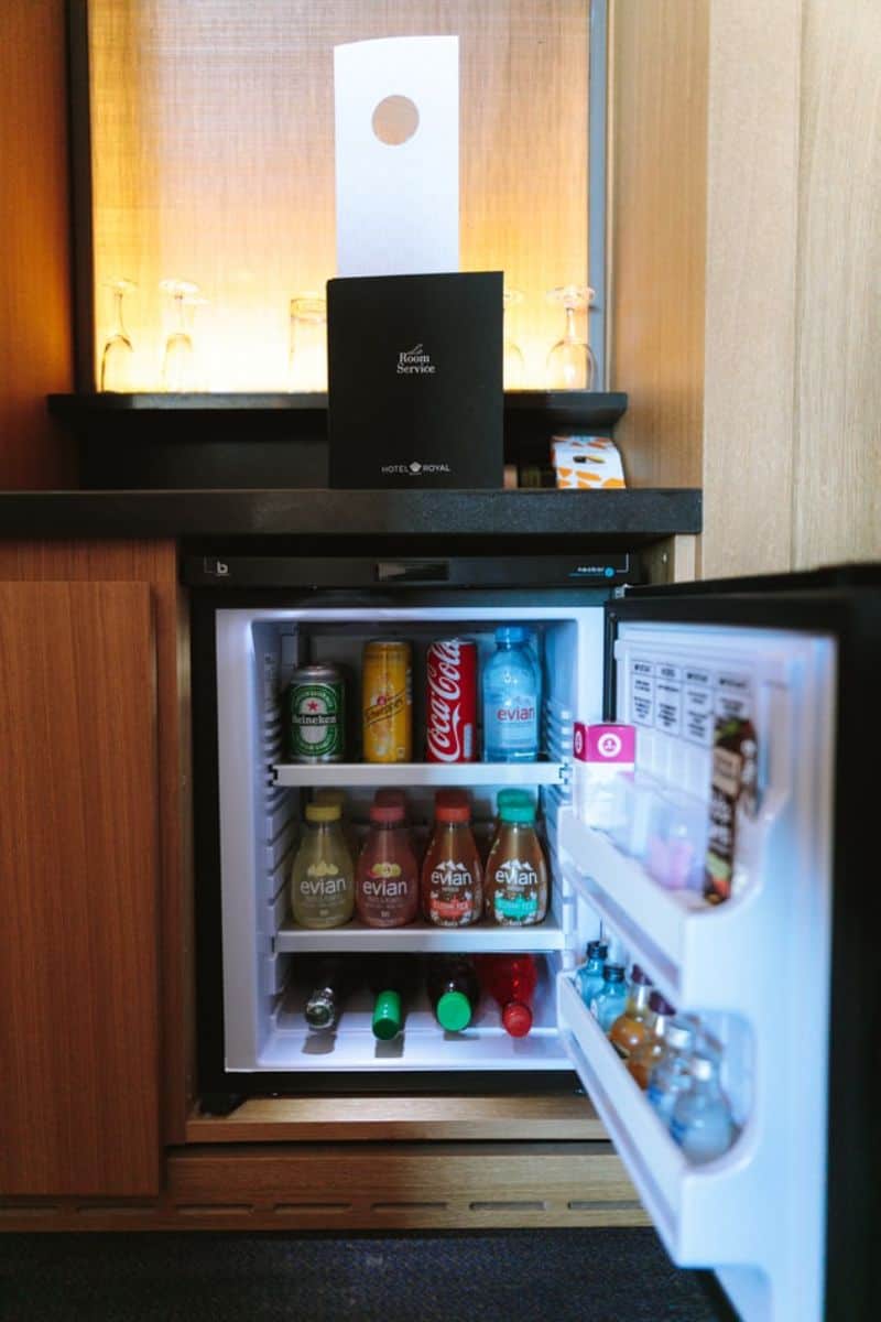 A mini bar set-up. Small refrigerator with lots of drinks inside.