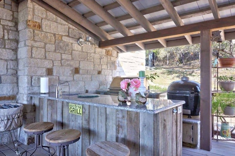 exposed stone-wall farmhouse covered patio with wood and marble bar and Kamado grill