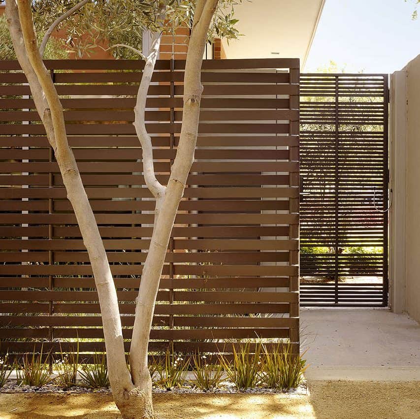 A woven steel screen, painted chocolate brown, surrounded with native plants