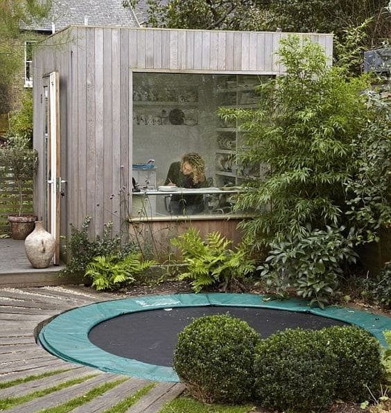 A small garden office with a large window to keep an eye on the children while playing outdoors