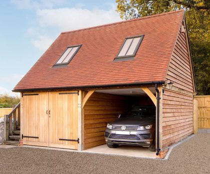 A wooden garage featuring an oak-frame structure, with a room above