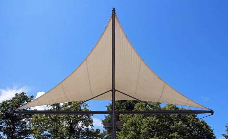 sun shade sail in a triangle against trees and a blue sky