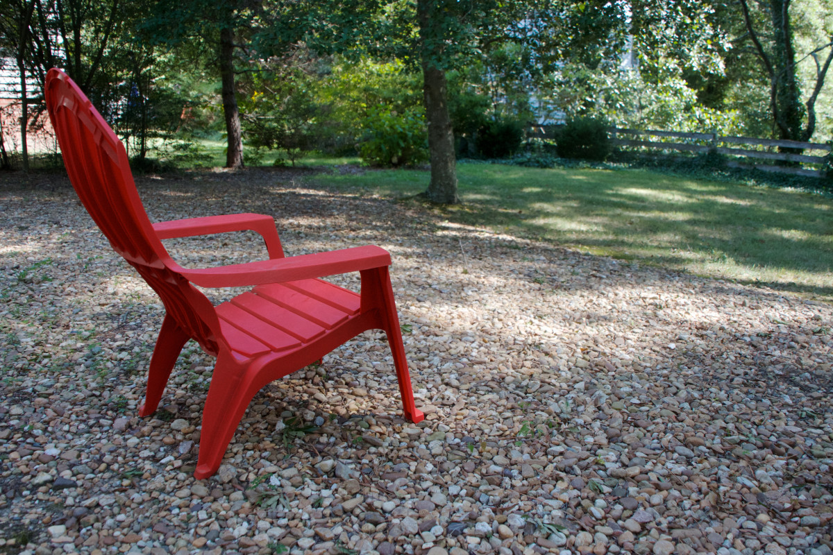 Red Adirondack chair on a gravel backyard