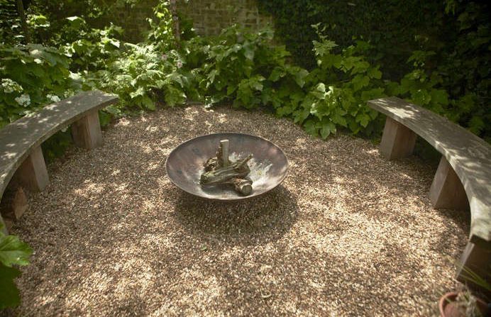 Surrounded by woodland, a gravel seating circle surrounds a fire pit.