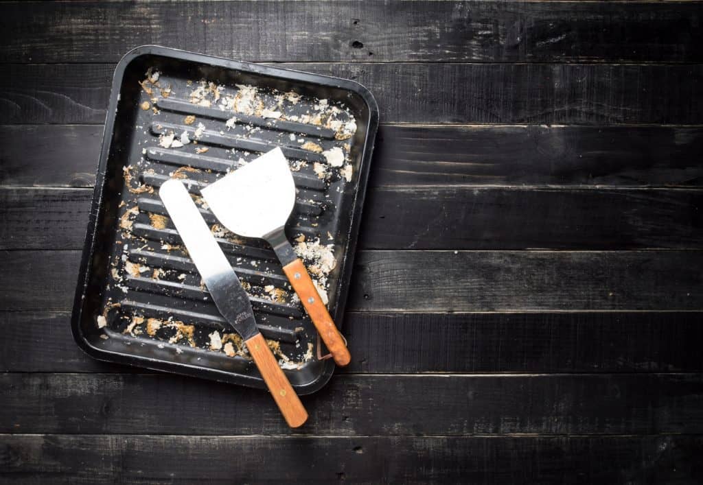 Metal baking tray and kitchen spatula with bread crumbs on dark wooden background,top view