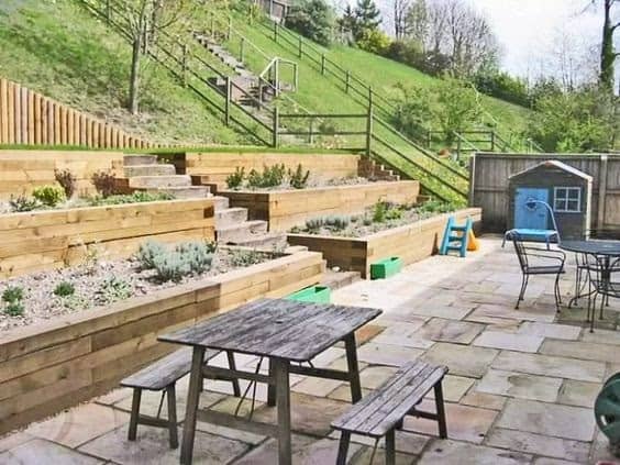 A sloped hill transformed into a cosy backyard by using tiered wooden planters and a picnic area 