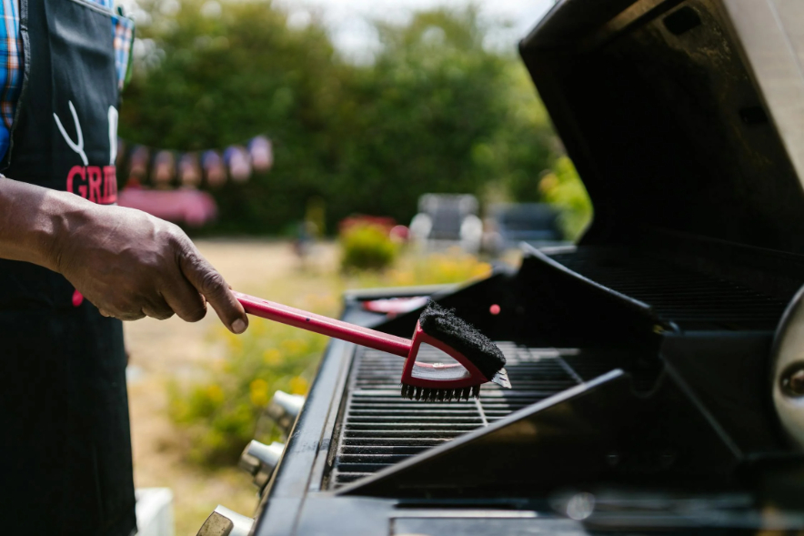 BBQ Checklist: Person cleaning BBQ grill grate with a brush.