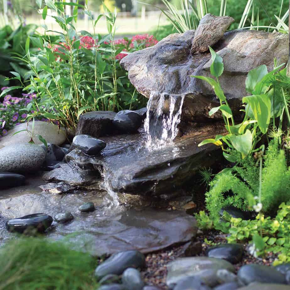 Mini garden waterfall with big stones and surrounding plants