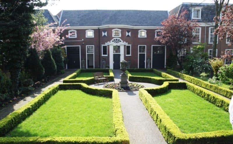 Outlined garden hedges outside a large house with a fountain or statue