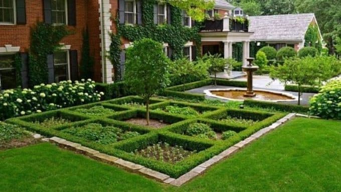 checkerboard hedge design outside a large house with a fountain