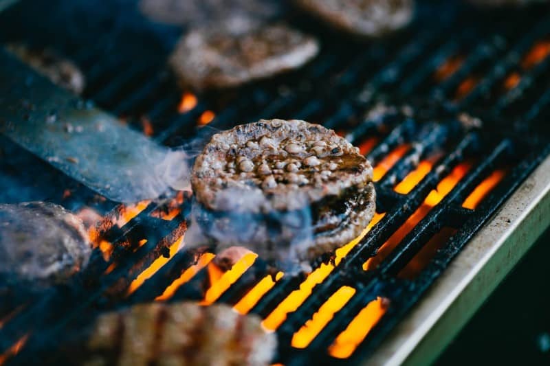 Burger patties being cooked on a grill with direct heat