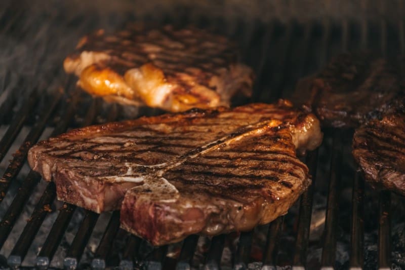 Large cuts of steaks on a grill with indirect heat