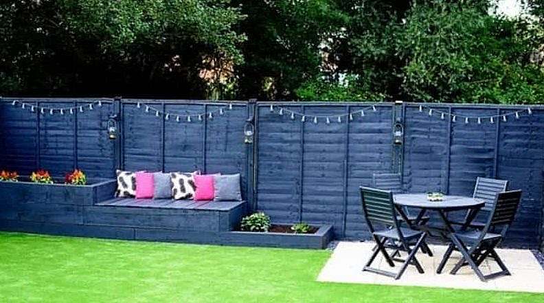 A fence painted in blue with a patio set and raised planters