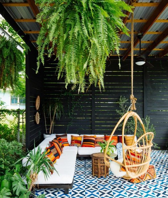 Covered patio with black fence and a hanging swing seat in a natural cane finish