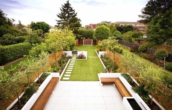 Modern long garden with a large seating area with a patio, a lush green lawn with stepping stones and a football field