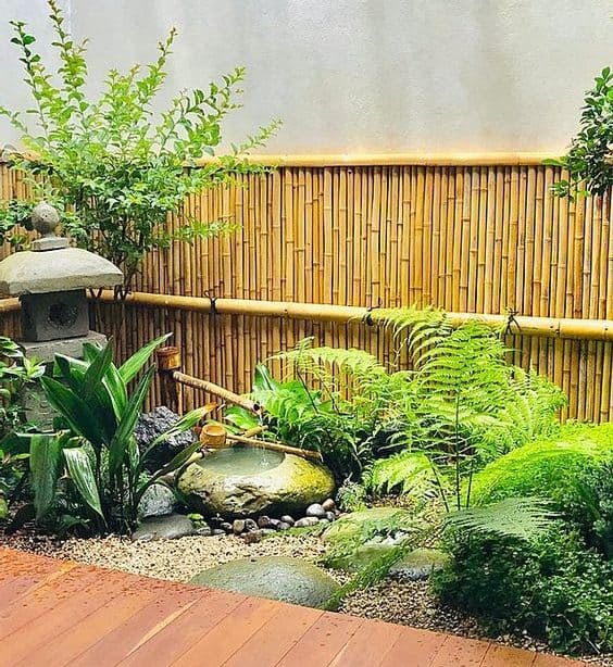 A miniature zen garden with some bamboo fencing, a stone water feature and leafy greenery