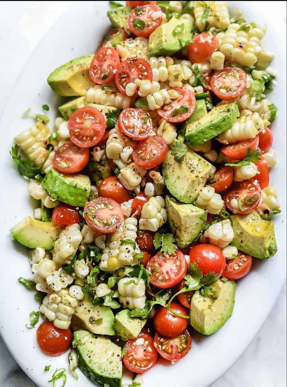 A healthy bowl of salad with corn, tomato, and avocado