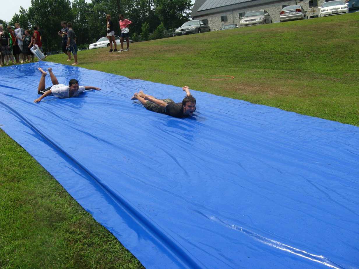 Children playing slip and slid in the garden with a big blue DIY slide