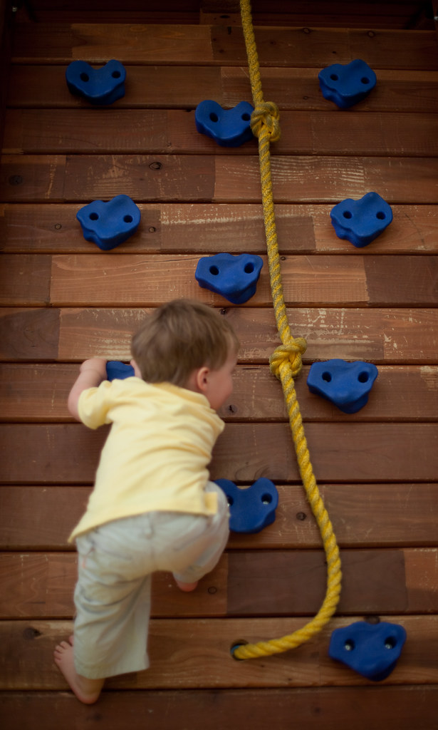 A kid climbing on a garden climbing wall