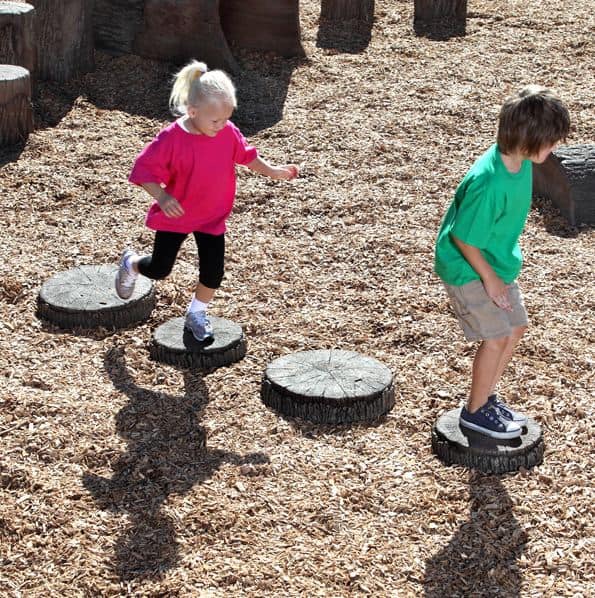 Two child stepping on tree-stump stepping stones