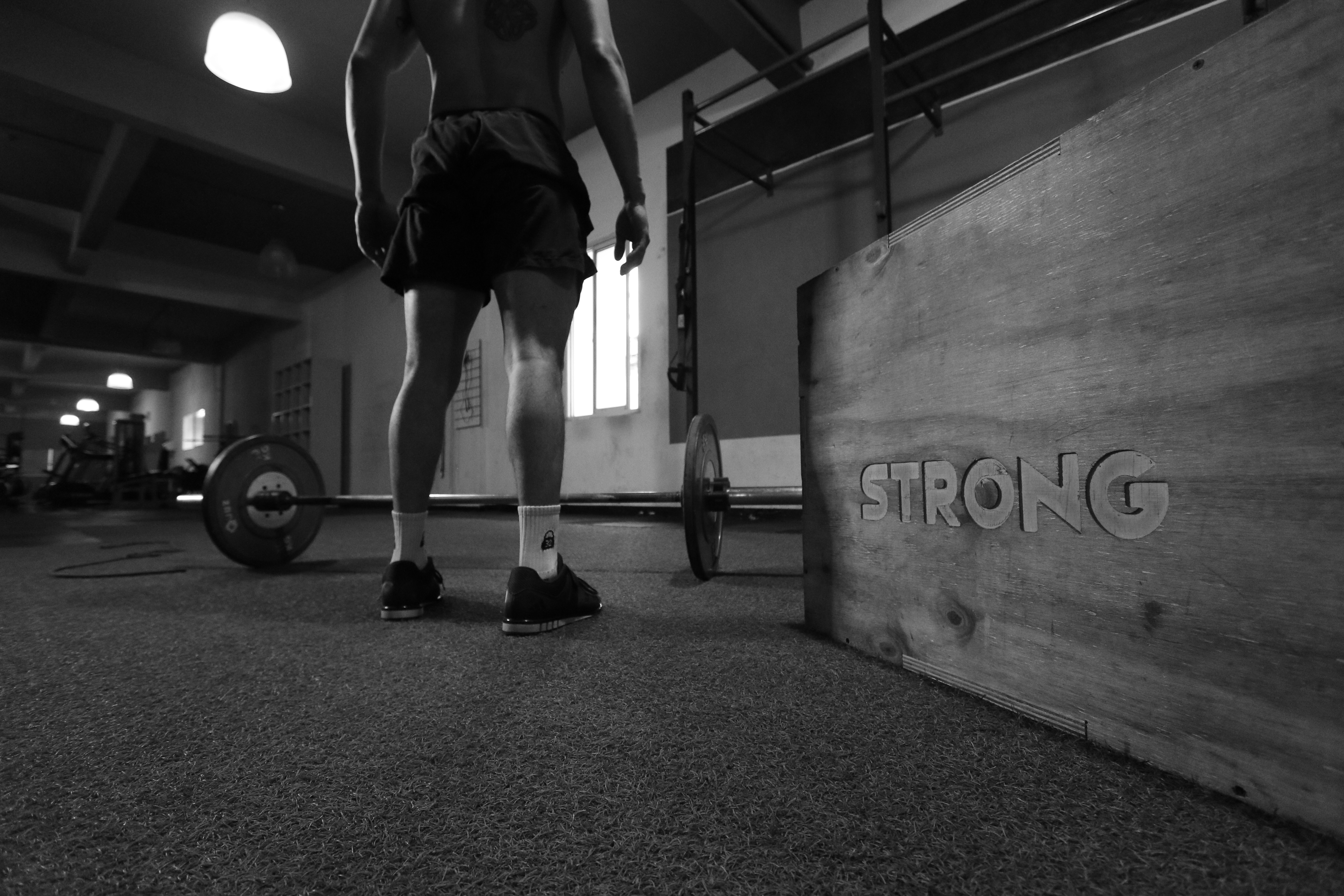 A greyscale photo of a man standing beside a barbell