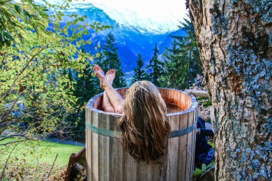 A woman enjoying an outdoor bath with a small wooden tub in the mountains
