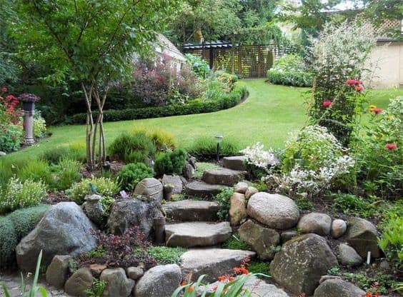 Large garden in slope with natural stone steps built into a rockery bed