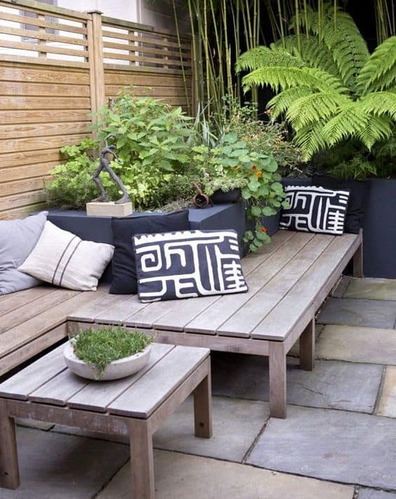 A tropical-themed corner garden with simple bench and some tropical plants