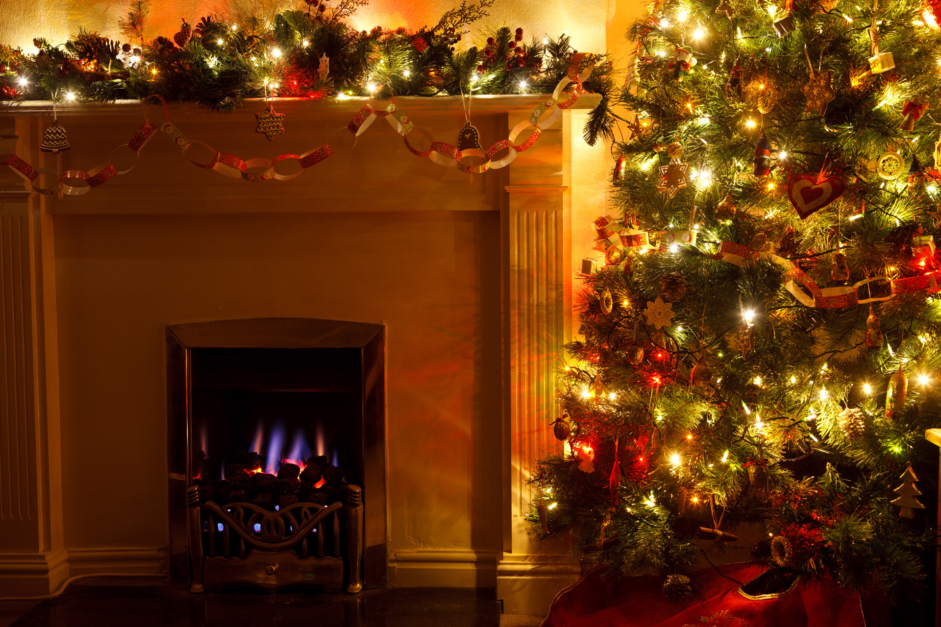 Indoor fireplace decorated with garlands and Christmas lights, with a tree on the side