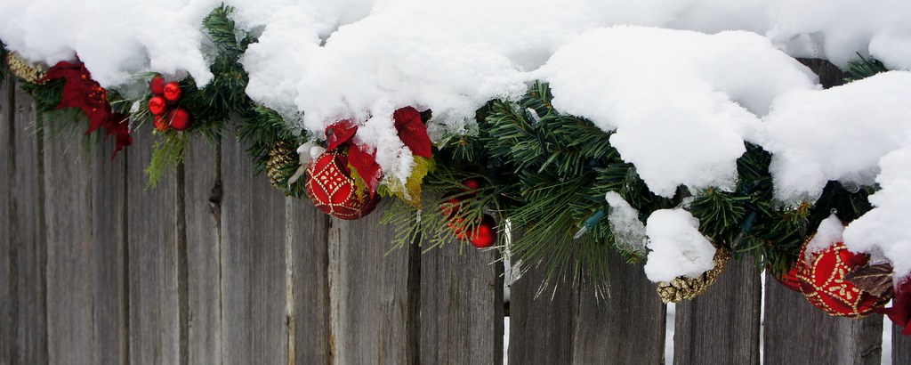 Wooden fence decorated with garlands and red Christmas ornaments