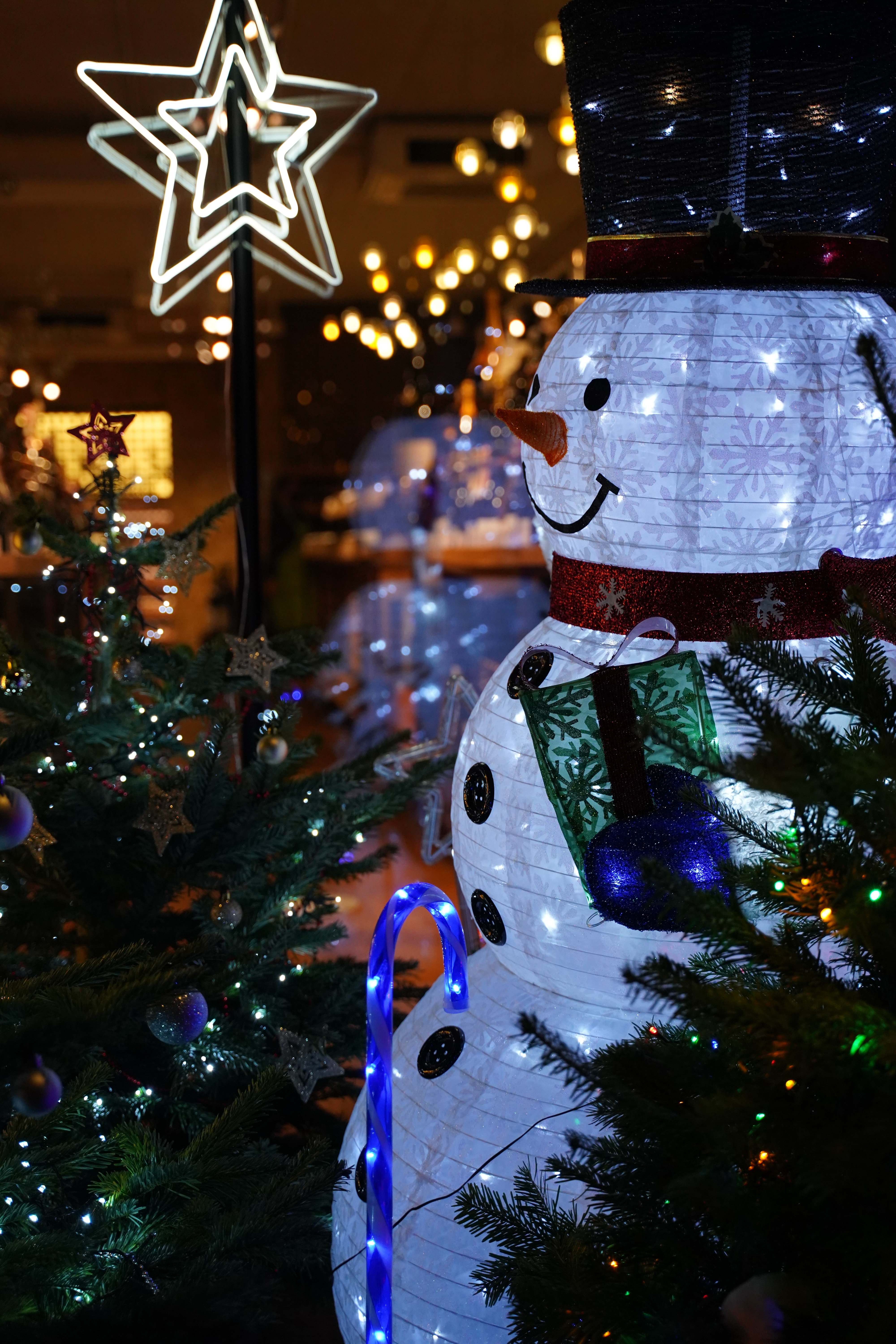 A large snowman beside a Christmas tree