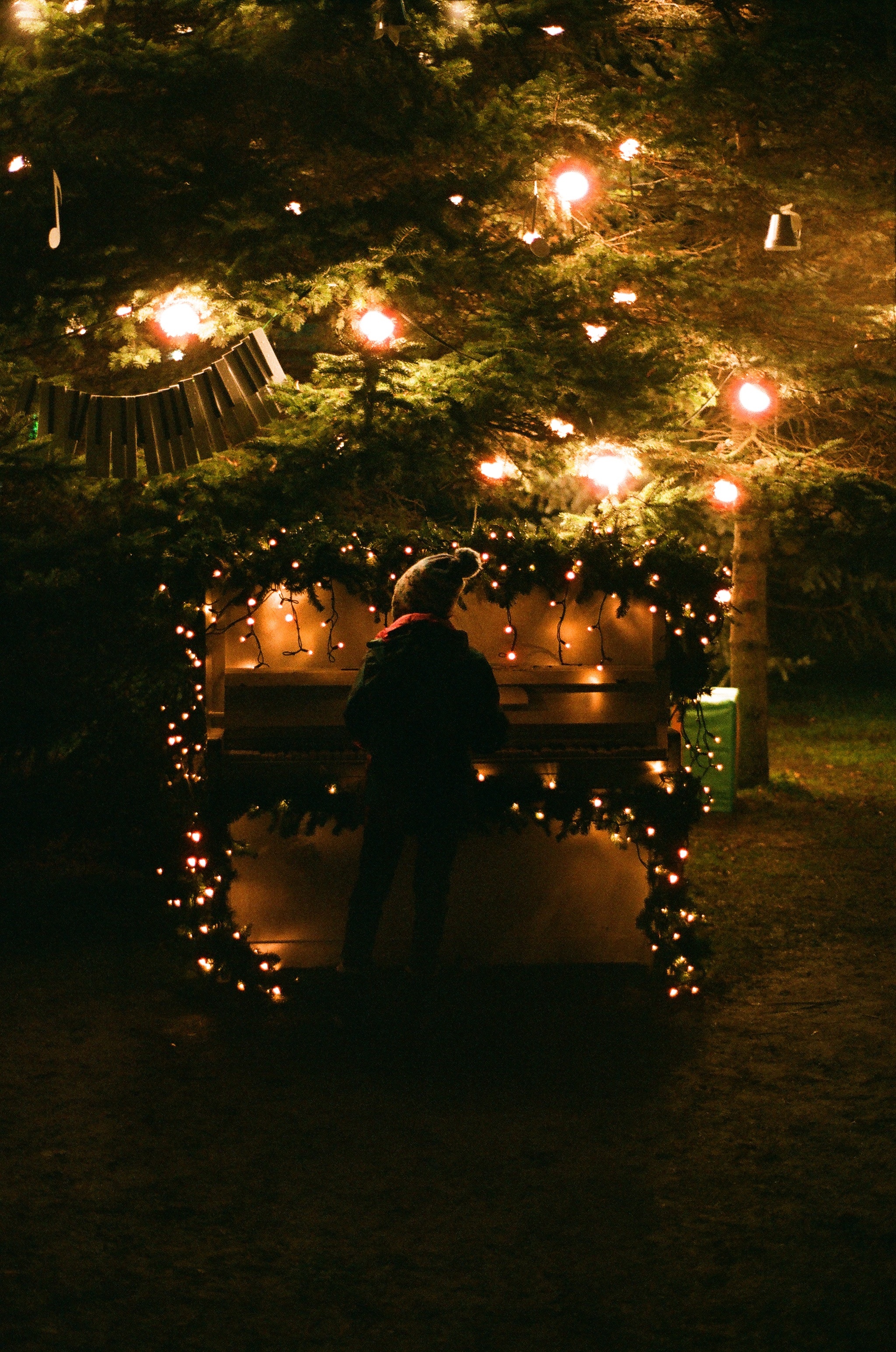 A person playing a decorated piano with garlands and Christmas lights