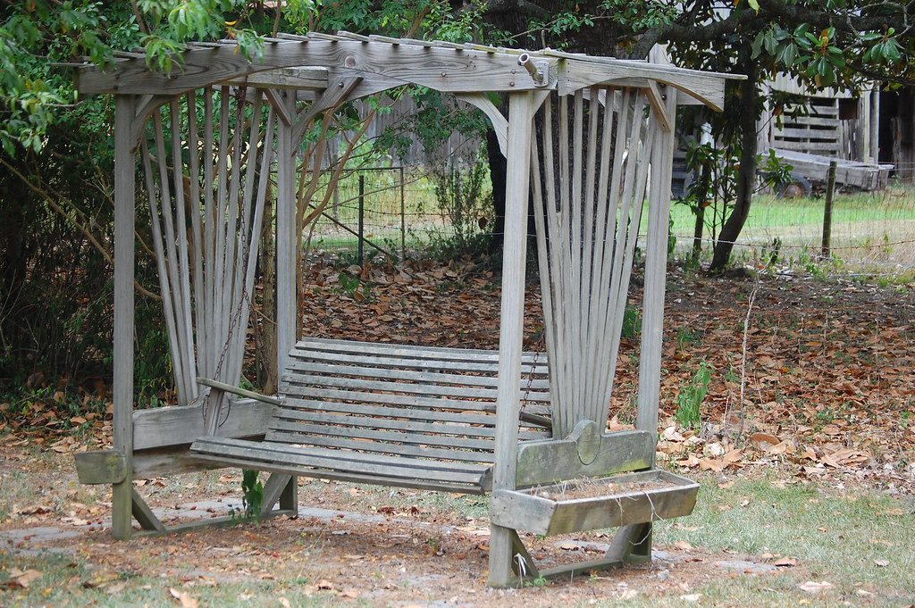 Weathered wooden arbour with swing bench.